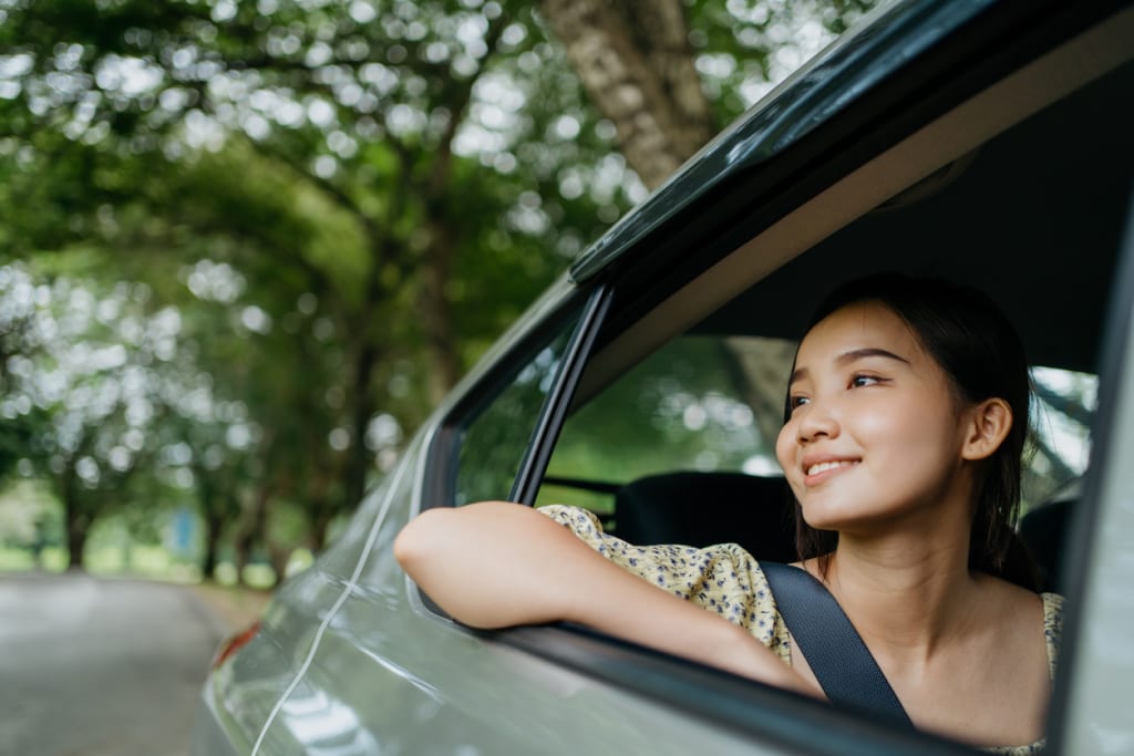 Smiling young woman looking out of car window on a scenic drive